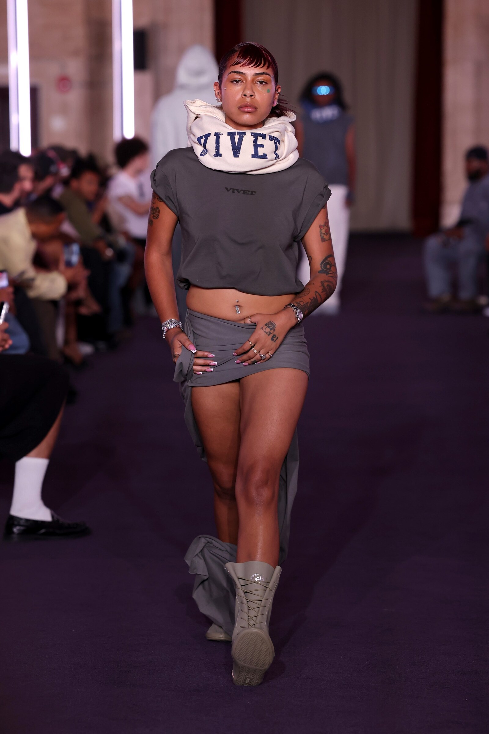 A model in a cropped charcoal VIVET top and matching shorts walks with the brand name wrapped around the neck