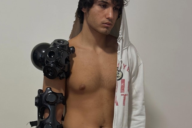 Shirtless model wears glossy black Ice Blade objects attached across one shoulder and forearm like futuristic armour